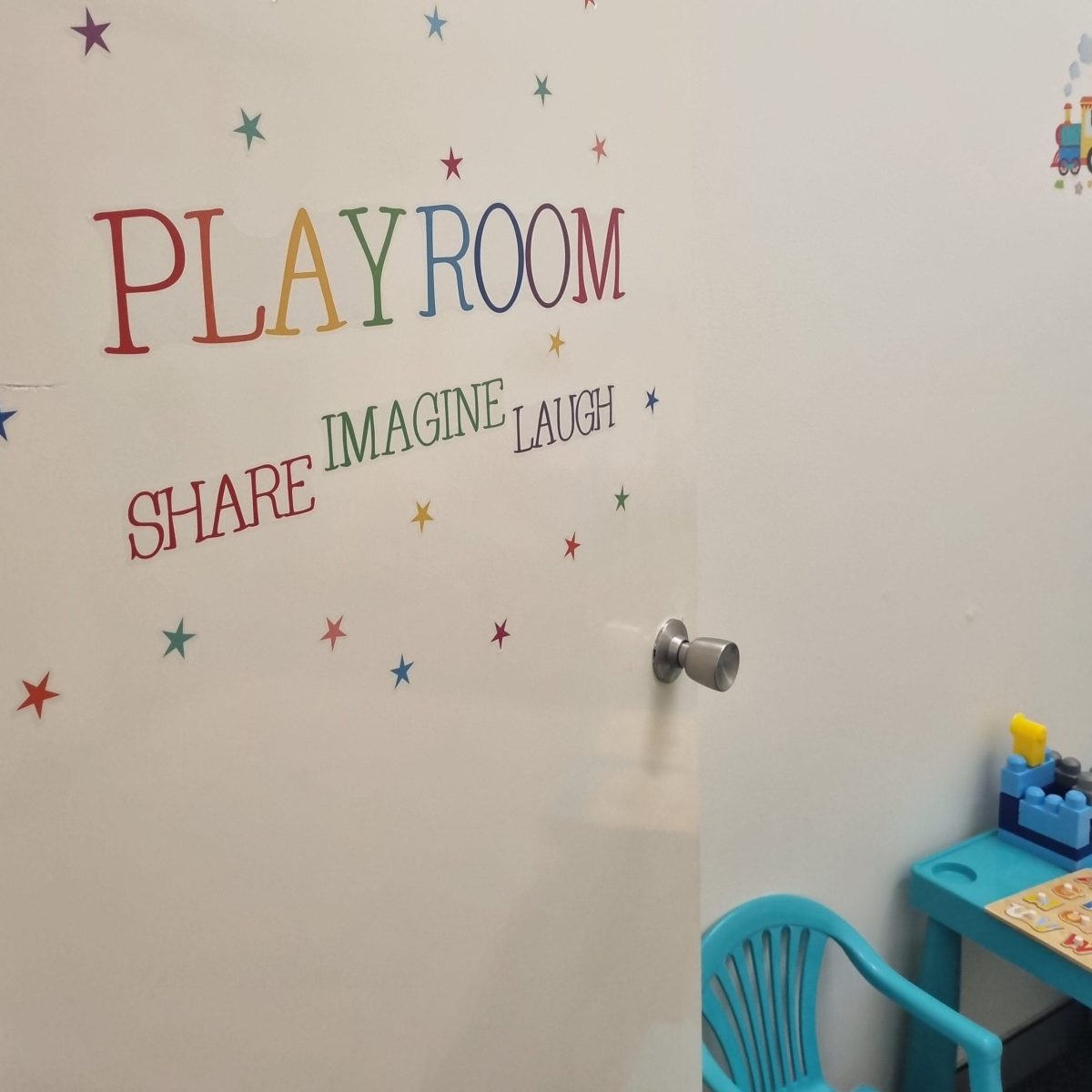 Photo shows a door to the Parent Pathways playroom in Armadale. The door has a colourful sign that says Playroom, Share, Imagine, Laugh.