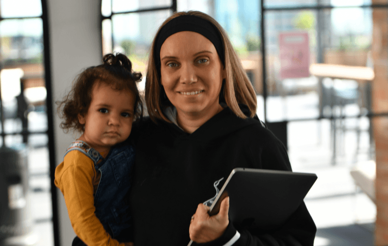 A mum is holding her young daughter and a laptop