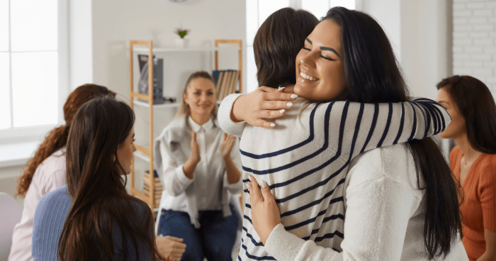 A young woman is being hugged in a group support.