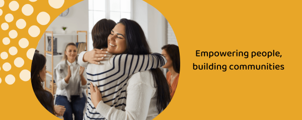 Empowering people, building communities_yellow Words read Empowering People, Building Communities with a yellow background, and a photo of a woman hugging another woman, being supported by a group of women.