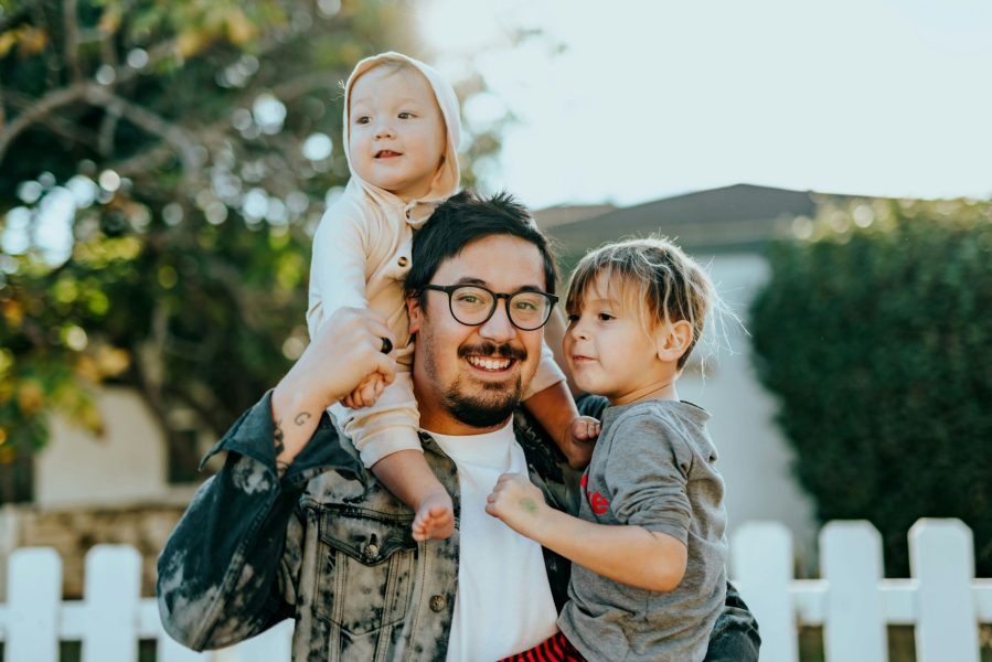 Man holding his two kids, one on his shoulders, the other in his arms.
